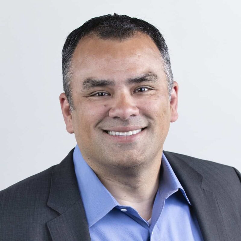 Man in grey suit and a blue shirt smiling